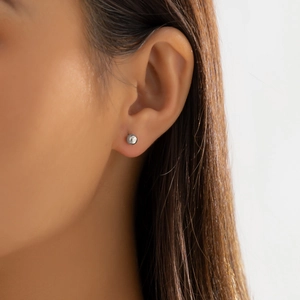Close-up of minimalist silver spherical stud earring worn on earlobe with polished finish