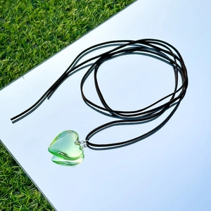 Detail of heart-shaped green pendant necklace with black cord on mirror and grass