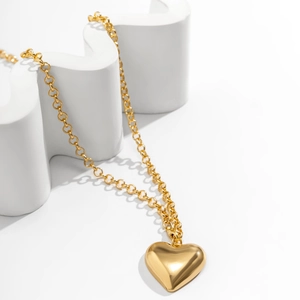 Close-up of polished gold heart pendant necklace on minimalist geometric white background