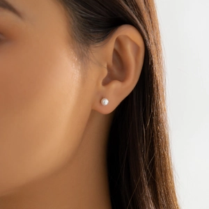 Close-up of minimalist pearl stud earrings worn by a model showing a refined retro style