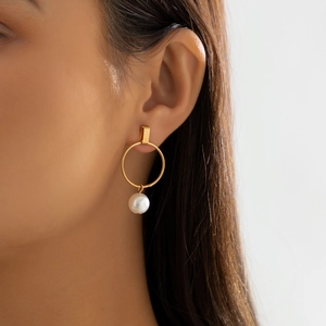 Close-up of a gold geometric earring with a white pearl drop worn by a model