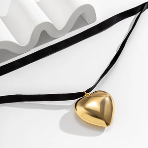 Macro shot of large polished gold heart pendant on a minimalist black velvet cord necklace