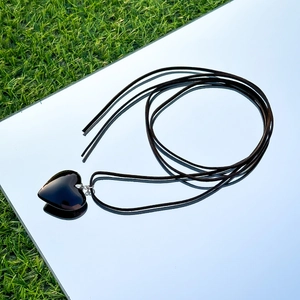 Macro detail of large black heart pendant on adjustable velvet cord with mirror reflection