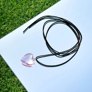 Close-up of a pink heart pendant on a black cord over a mirror with grass reflection