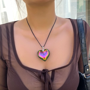 Close-up of iridescent heart pendant on a black cord necklace worn by a model