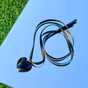 Detail of a large black heart pendant on a black satin cord over a reflective sky background