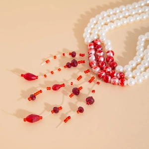 Macro detail of gothic choker featuring white pearls and red crystal beaded tassels