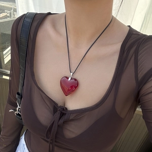 Close-up of a large red heart-shaped resin pendant on a black cord worn by a model
