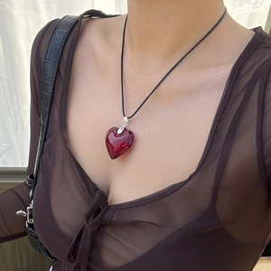 Minimalist red heart pendant necklace on a black cord worn by a female model