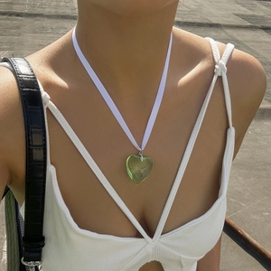 Close-up of a green heart glass pendant on a white satin cord worn by a model outdoors