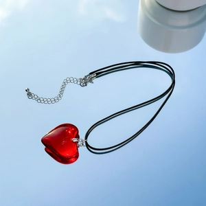 Detail of a red translucent heart pendant on a black cord with silver extension chain