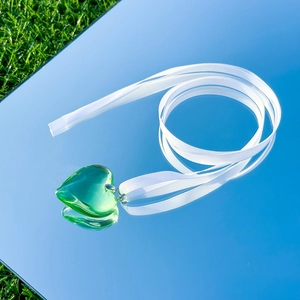 Detail of a green heart-shaped glass pendant on a white ribbon with silver buckle