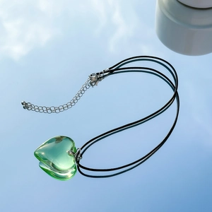 Detail of green transparent heart pendant with adjustable black cord on reflective base