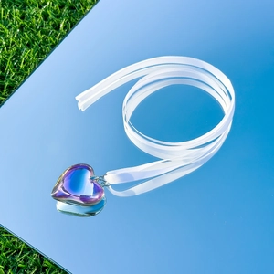 Detail of iridescent heart pendant on white ribbon necklace reflecting on a mirror