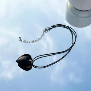 Close-up of polished black heart pendant on a woven cord with adjustable silver chain