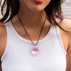 Macro detail of a translucent pink heart pendant on a black cord worn by a model