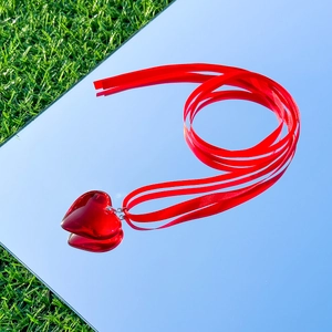 Macro detail of a vibrant red heart pendant necklace with a red silk ribbon on a mirror