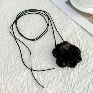 Detailopname van een 3D zwarte stoffen roos choker met lang koord op wit gebreid vlak