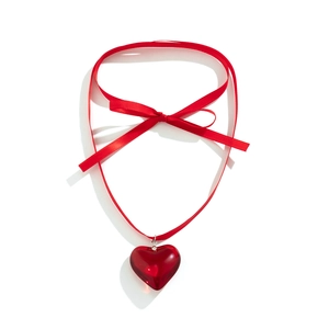 Macro detail of large red heart pendant with elegant red satin ribbon bow necklace