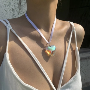Detailed view of an iridescent heart pendant on a white ribbon cord worn by a model
