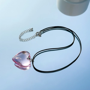 Macro detail of a pink glass heart pendant on a black cord over a blue mirror surface