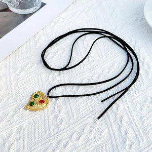 Detail of vintage heart pendant with colorful gemstones on black cord over lace