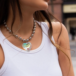 Detailed view of an iridescent heart pendant on a silver ball chain worn by a model
