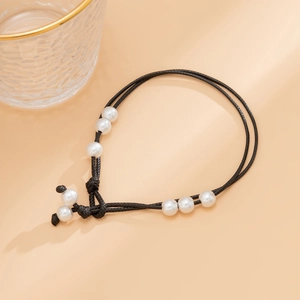 Detalle de tobillera de cuerda negra tejida ajustable con elegantes perlas blancas