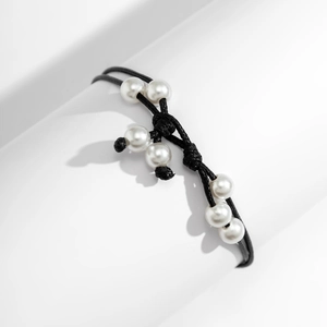 Detalle de tobillera de cordón negro trenzado con perlas de imitación blancas en base