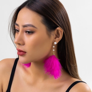 Close-up of rose red feather earrings with faux pearls worn by a model on light background