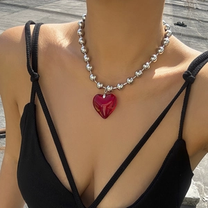 Detail of a large red heart pendant on a silver beaded chain worn by a model outdoors