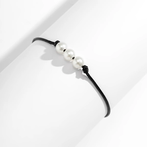 Detalle de pulsera de cordón negro trenzado con tres perlas blancas brillantes sobre un soporte