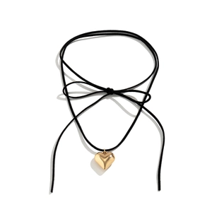 Detailed close-up of a large gold heart pendant on a black suede choker with bow tie