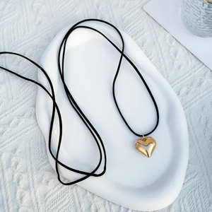 Close-up of golden 3D heart pendant on black cord over white ceramic display tray