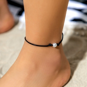 Primer plano de una tobillera con perla única y cordón negro trenzado estilo playero