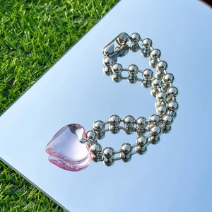 Detail of pink heart pendant on double silver bead chains with mirror sky reflection