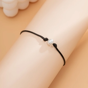 Vista macro de una pulsera minimalista de cordón negro con una única perla blanca