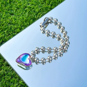Macro shot of iridescent heart pendant on silver bead chain over mirrored surface