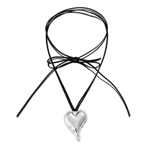 Close-up of molten silver heart pendant with black cord bow on white background