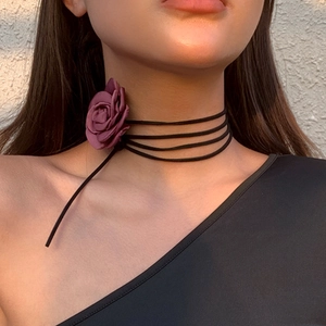 Detail van een meerlaagse fluwelen choker met een donkerrode satijnen roos om de nek