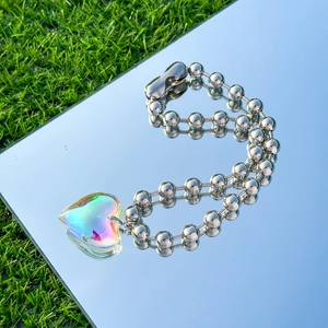 Macro view of silver bead chain and iridescent heart pendant reflecting outdoor light