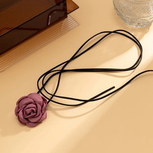 Detail van donkerpaarse satijnen roos aan een zwarte fluwelen lint choker ketting