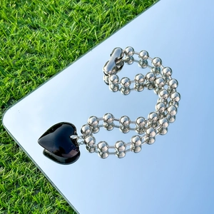 Detail of a black heart pendant with double-row silver bead chain on a mirror surface