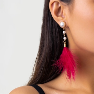 Close-up of elegant long pearl earrings with vibrant magenta feather tassel on model