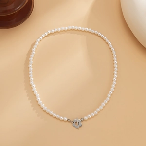 Gros plan d'un collier de perles blanches avec un fermoir fleur en argent sur fond beige