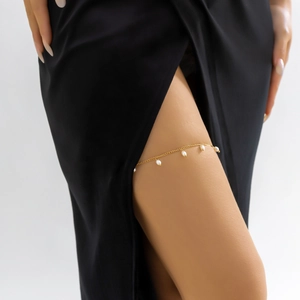 Detail of elegant gold-tone thigh chain with small white pearls on a model wearing black