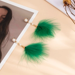 Detail of green feather tassel earrings with imitation pearls on a beige surface