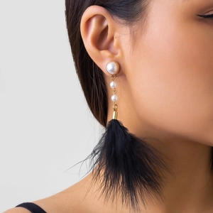 Detail of vintage earring featuring white pearls, gold chains and black feather tassels