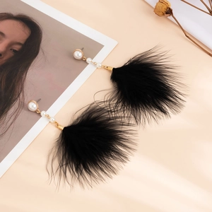 Detailed close-up of long bohemian earrings with gold accents, white pearls and black feathers
