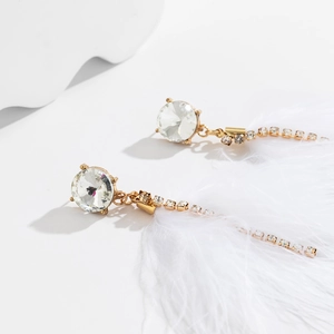 Detail of elegant gold earrings with white feathers, clear crystals and tassel chains